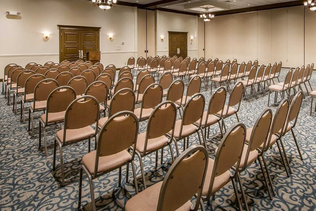 Rows of empty beige chairs are arranged facing the front in a carpeted conference room - Villas by the Sea Resort, Jekyll Island
