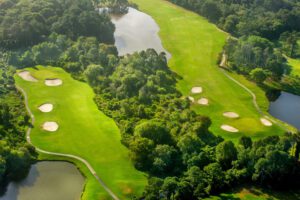 Aerial view of a lush green golf course with multiple sand bunkers, fairways, winding paths, and several water features surrounded by dense trees and vegetation. - Villas by the Sea Resort, Jekyll Island